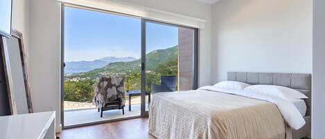 A bedroom with a bed, a chair, and a view of a mountainous landscape through a large sliding glass door.
