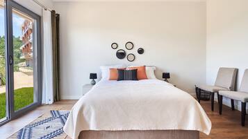 Un dormitorio con una cama grande, dos mesitas de noche, una silla, una alfombra estampada y vistas a través de un ventanal.
