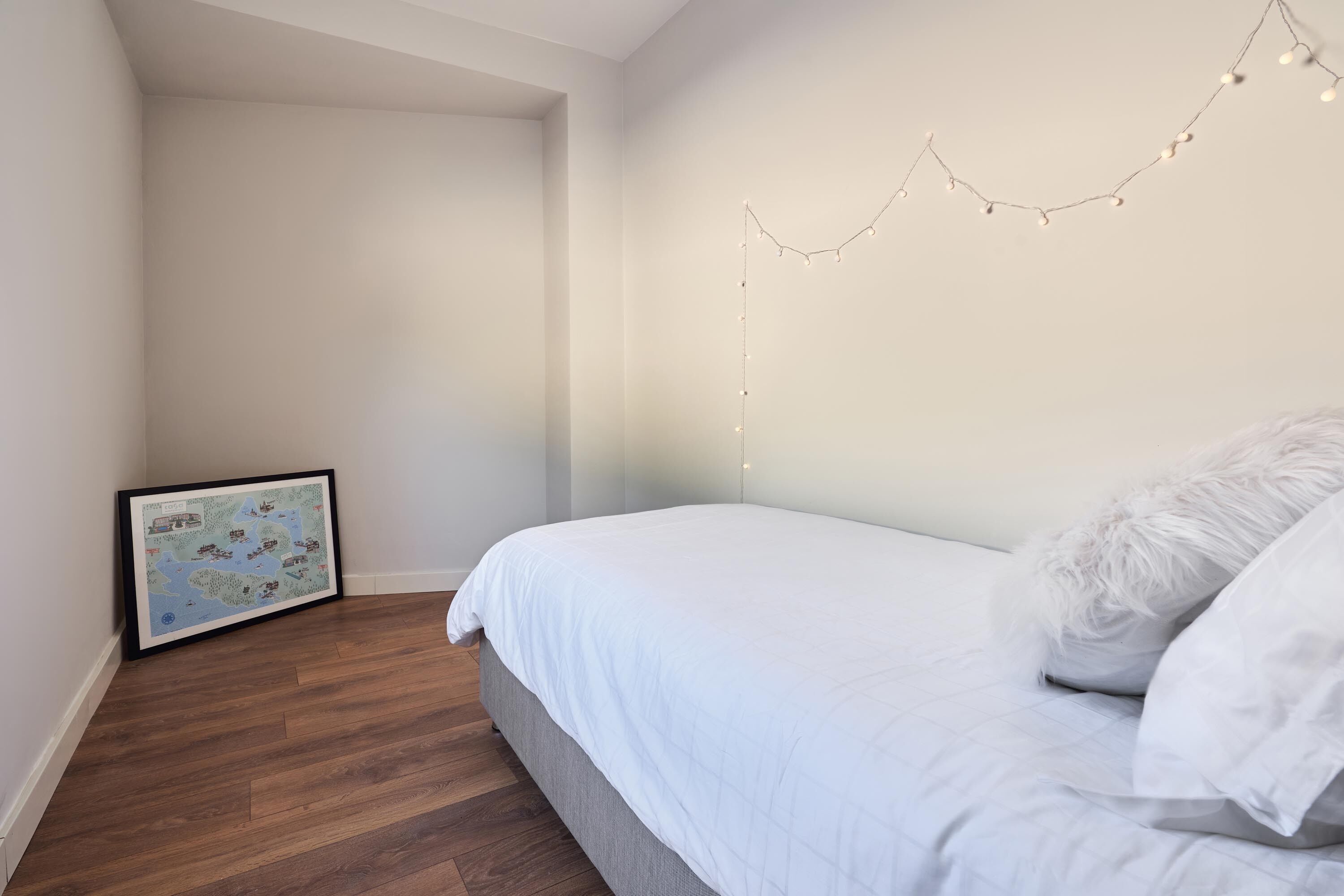 A bedroom with a bed, a framed map on the wall, and string lights.