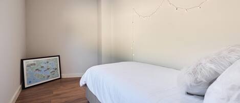 Un dormitorio con cama, un mapa enmarcado en la pared y luces de cadena.