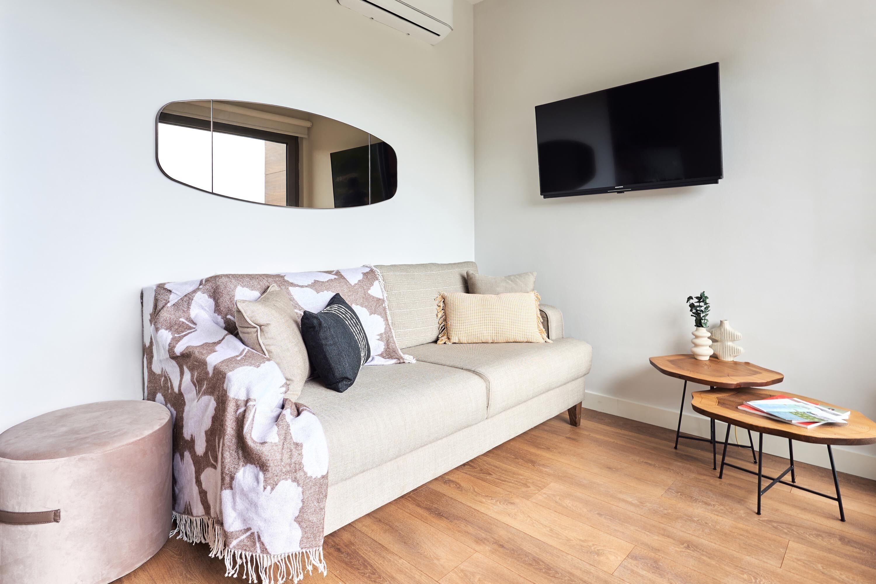 A modern living room with a sofa, a round wooden table, a television mounted on the wall, and a round rug.
