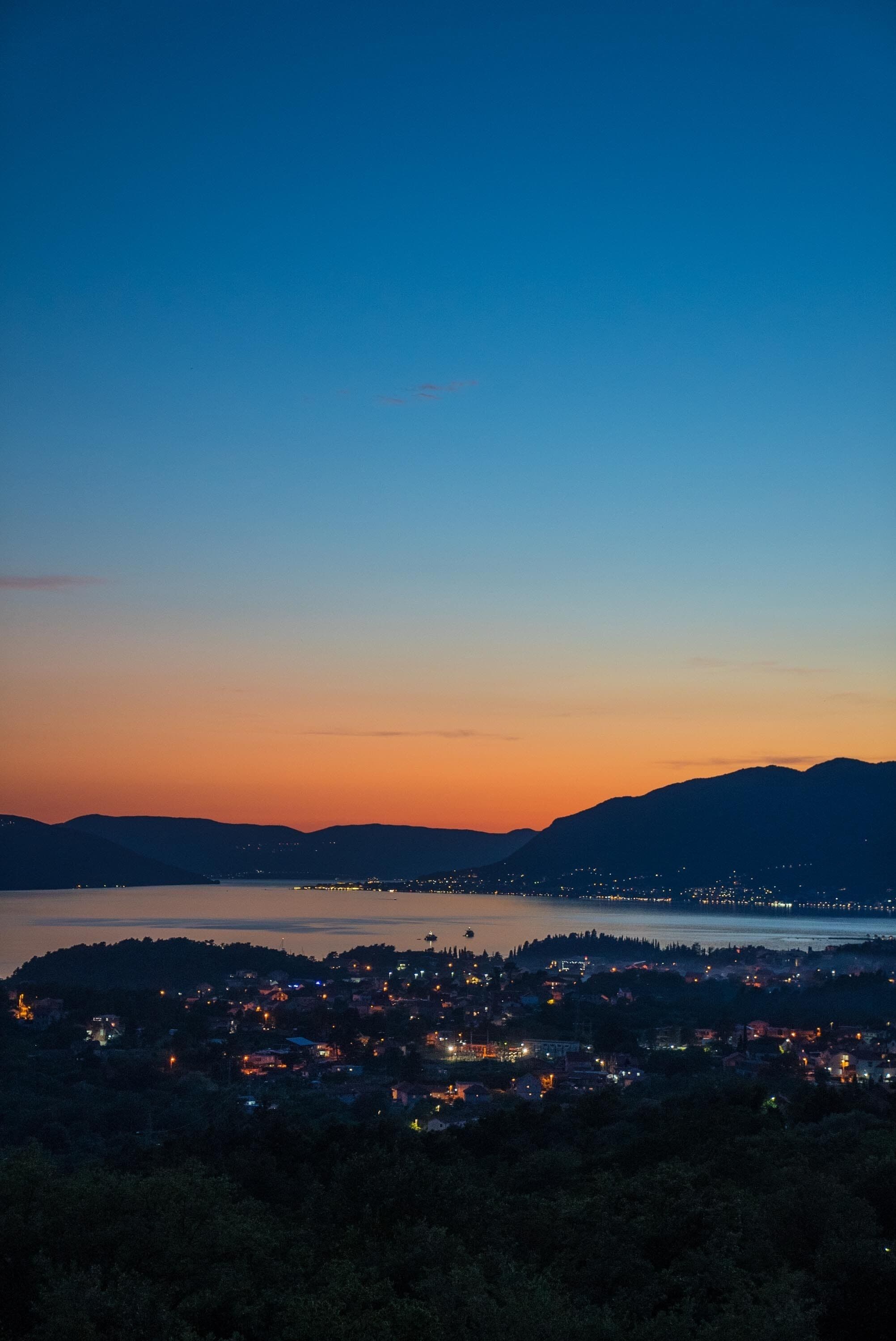 A coastal town at dusk with a view of the sea and mountains.