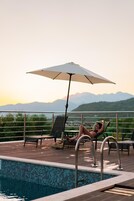 Área da piscina com vista para montanhas, uma espreguiçadeira e um guarda-sol.