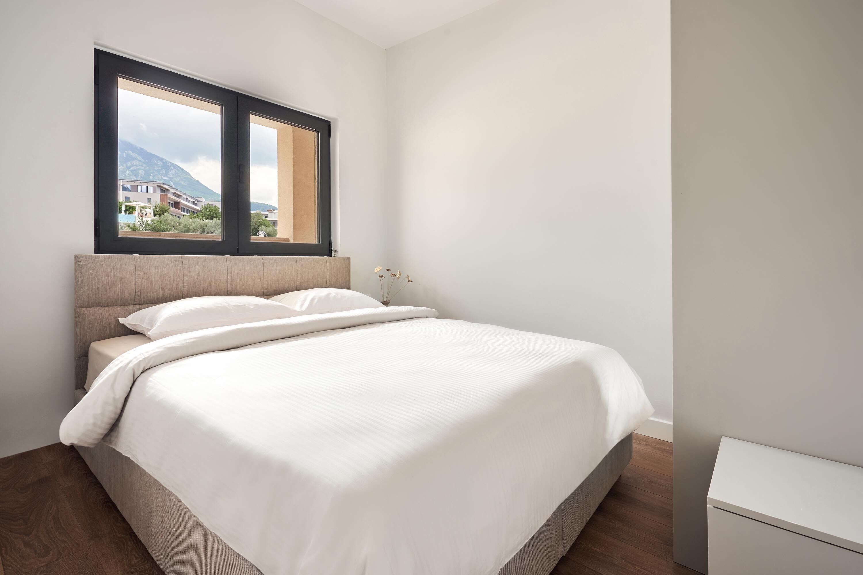 A bedroom with a bed, a window, and a view of buildings.