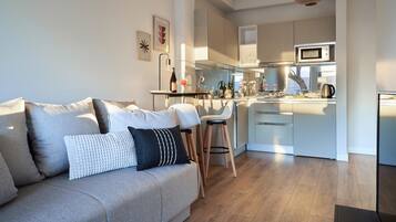Una sala moderna con un sofá, una mesa de centro y una zona de cocina con microondas y hervidor.