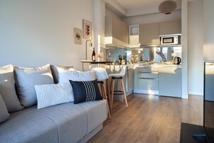 Una sala moderna con un sofá, una mesa de centro y una zona de cocina con microondas y hervidor.