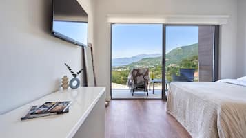 Ein Schlafzimmer mit Bett, Schreibtisch, Stuhl und Blick auf eine gebirgige Landschaft durch eine Schiebetür.