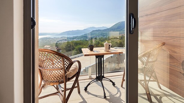 A balcony with wicker chairs, a table, and a view of a mountainous landscape. -  Casa Collection (Kotor)