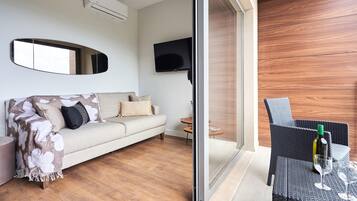 Un salon moderne avec un canapé, un téléviseur à écran plat et une porte vitrée donnant sur un espace extérieur agrémenté d'une table et de chaises en osier.