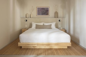 A minimalist bedroom with a wooden bed frame, white bedding, and a single bedside table with a lamp. - Drift Palm Springs (PALM SPRINGS)