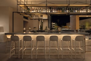 A bar area with a long counter, multiple stools, and a variety of bottles on shelves.