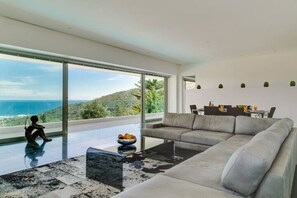 Uma sala de estar moderna com um sofá grande, uma mesa de vidro e vista para o mar.