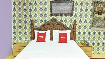 A neatly made bed with a red and white bedspread, two red pillows with the OYO logo, a wooden headboard, and patterned wallpaper.