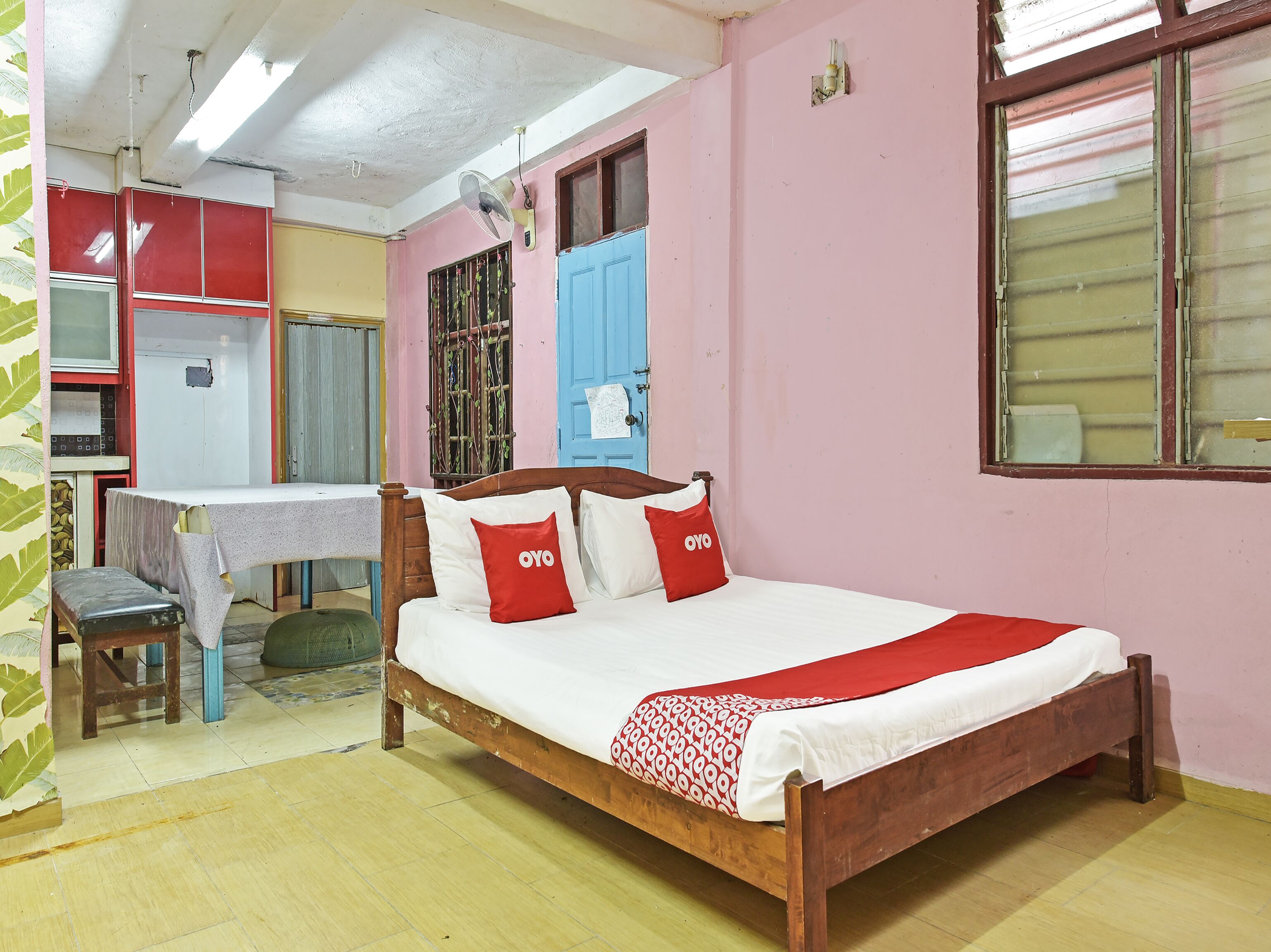 A room with a wooden bed, a desk, a chair, and a window with a blue shutter.