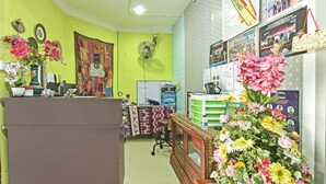 Zona de recepción con un mostrador, un gran arreglo floral y diversas decoraciones de pared, incluyendo carteles y un tapiz.