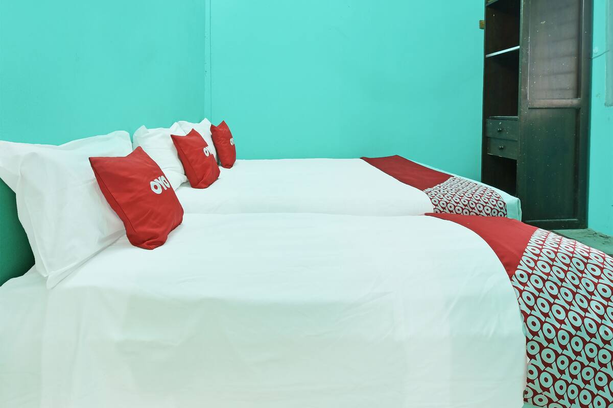 A bed with white and red bedding, a patterned blanket, and a wardrobe against a teal wall.