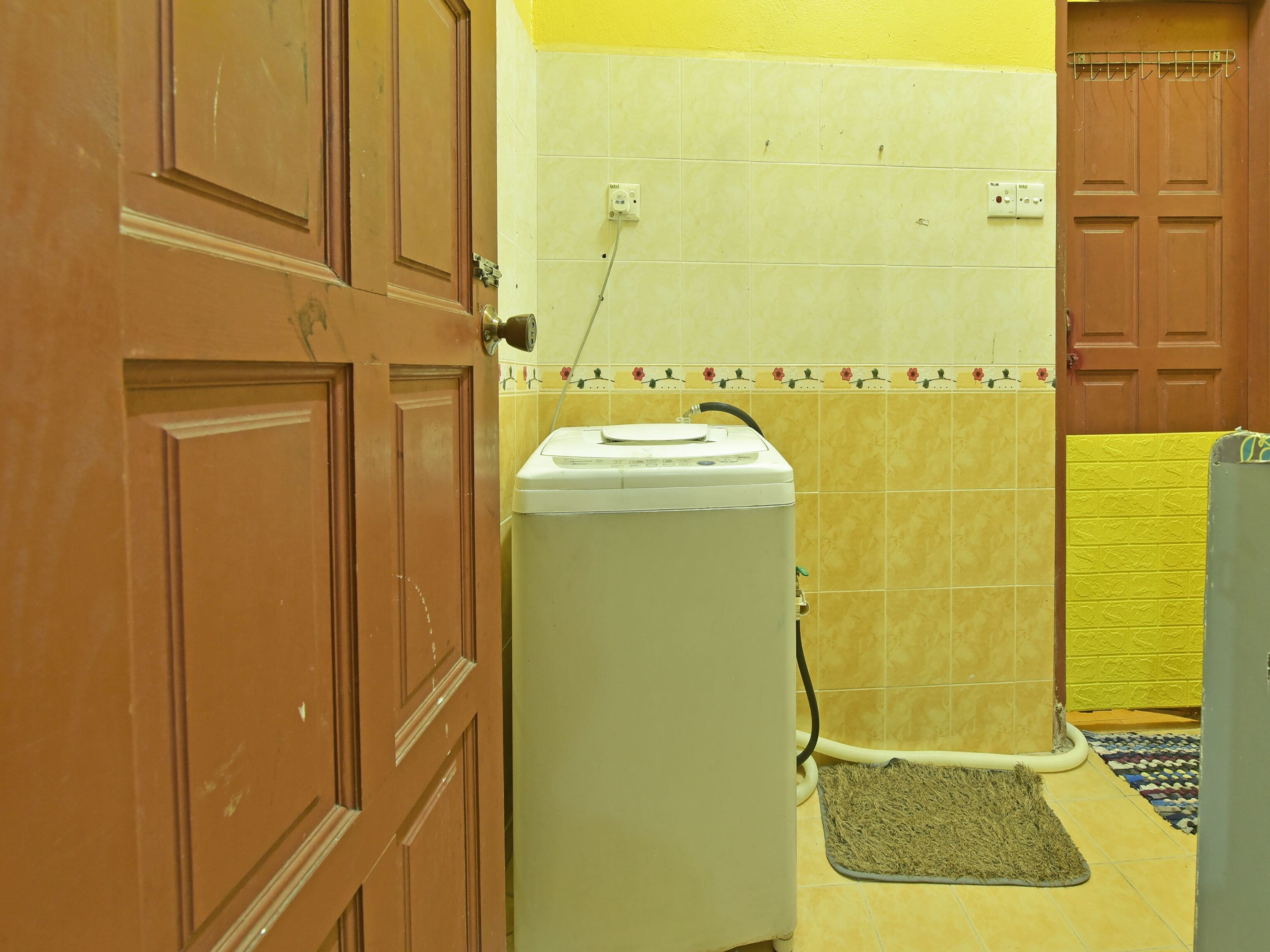 A laundry room with a washing machine, a yellow wall, and a door.