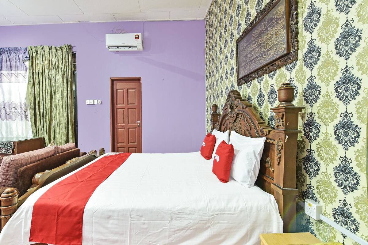 A bedroom with a large bed, a wooden headboard, a red and white bedspread, and patterned wallpaper.