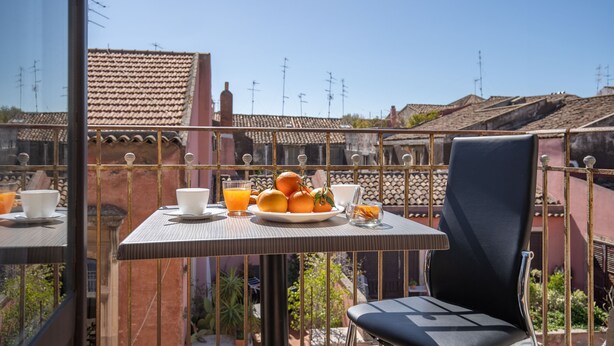 A balcony with a table set for breakfast, including oranges and juice, and a chair.