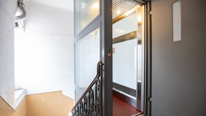 A modern elevator with glass doors, a metal handrail, and a red carpet leading to the elevator.
