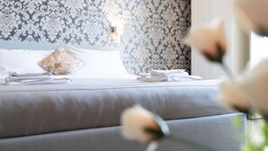 A neatly made bed with folded towels, a floral pillow, and a patterned wallpaper headboard.