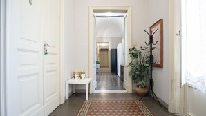 A hallway with a checkered floor, a white door with the number 6, a white bench with two decorative items, and a potted plant.
