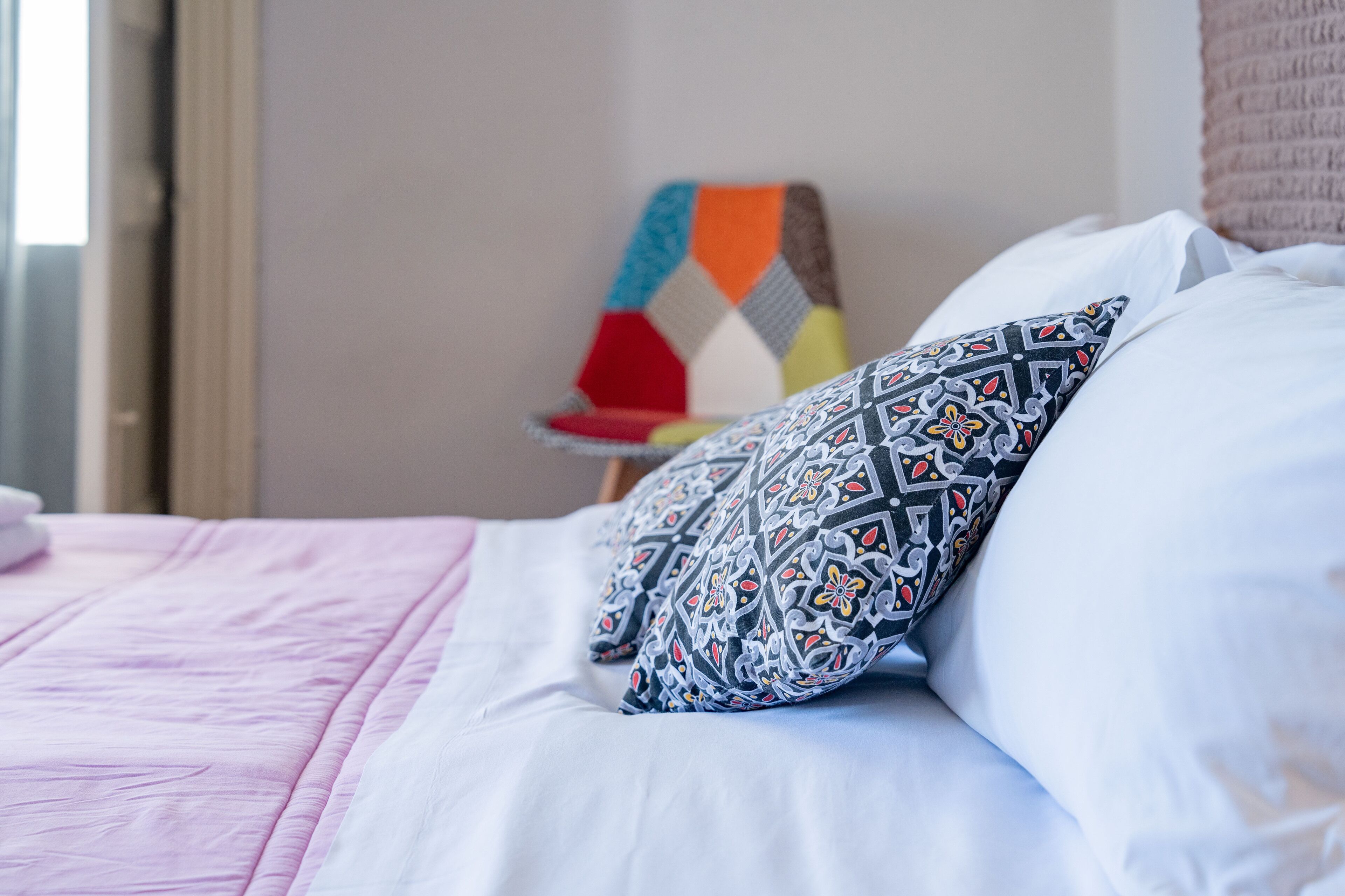 A neatly made bed with patterned pillows and a pink blanket.