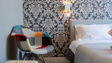 A hotel room with a patterned wallpaper, a bed with white linens, and a colorful chair.