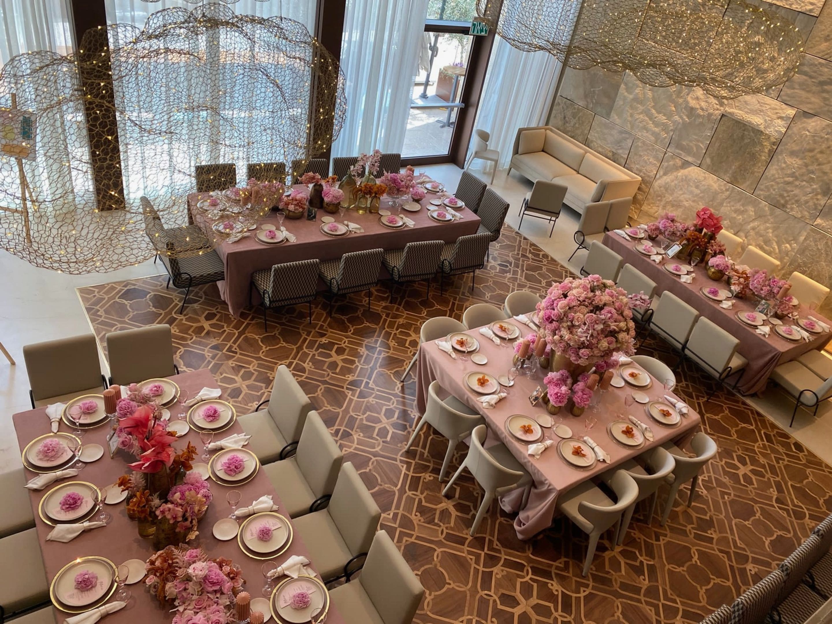 Un comedor espacioso con varias mesas dispuestas para un evento formal, con elegantes vajillas y centros de mesa florales.