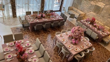 Un comedor espacioso con varias mesas dispuestas para un evento formal, con elegantes vajillas y centros de mesa florales.