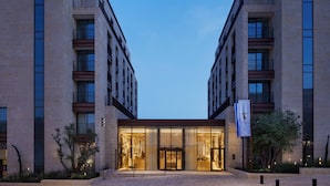 A modern hotel entrance with a glass facade, a central entrance, and a flag. - Theatron Jerusalem Hotel & Spa - MGallery Collection (Jerusalem)
