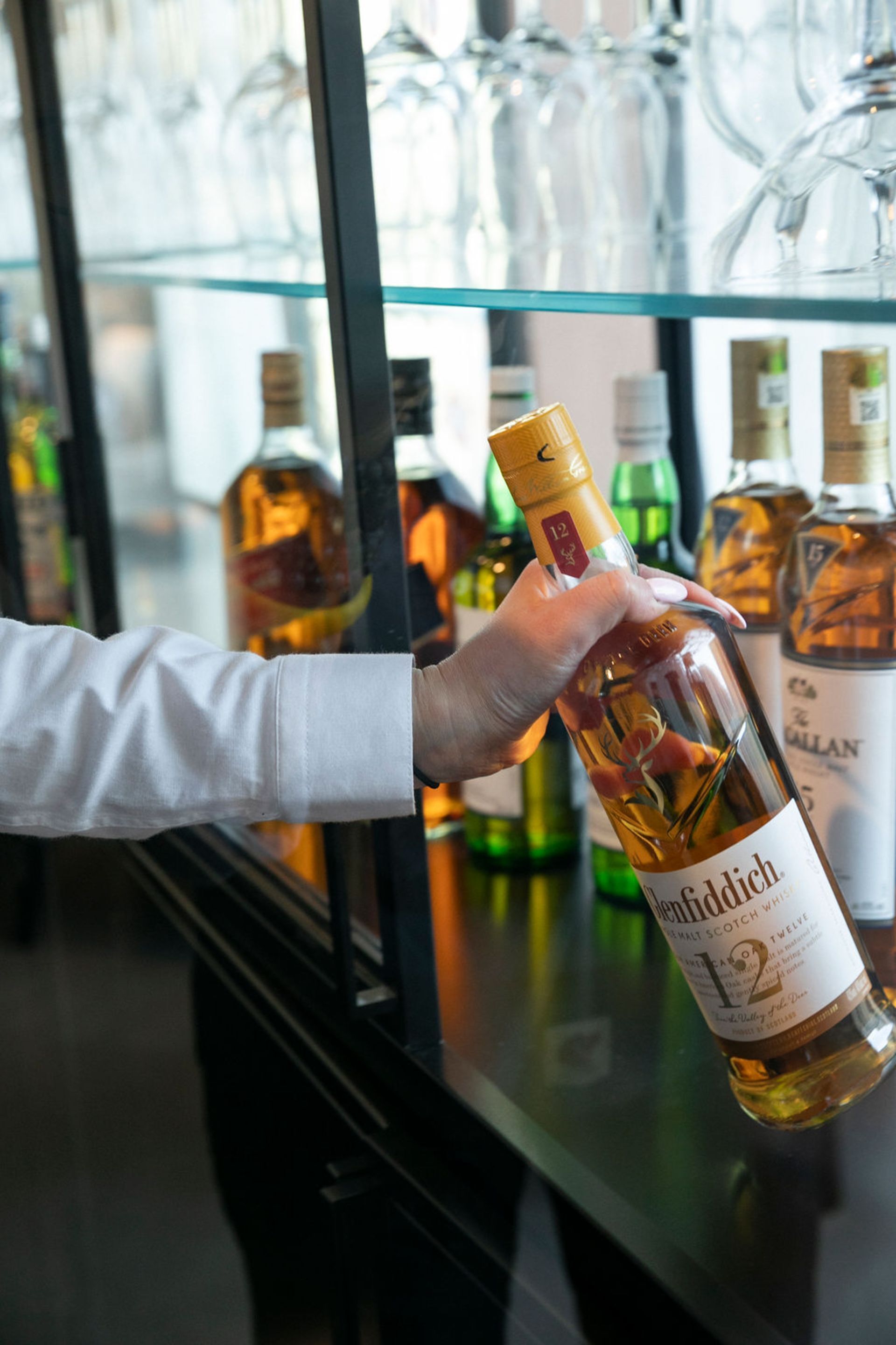 Eine Hand hält eine Flasche Whisky mit dem Etikett 'Ben Nevis 12 Year Old Scotch Whisky'.