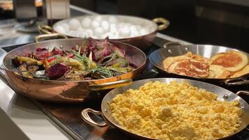 A buffet with various dishes including scrambled eggs, roasted vegetables, and pancakes.