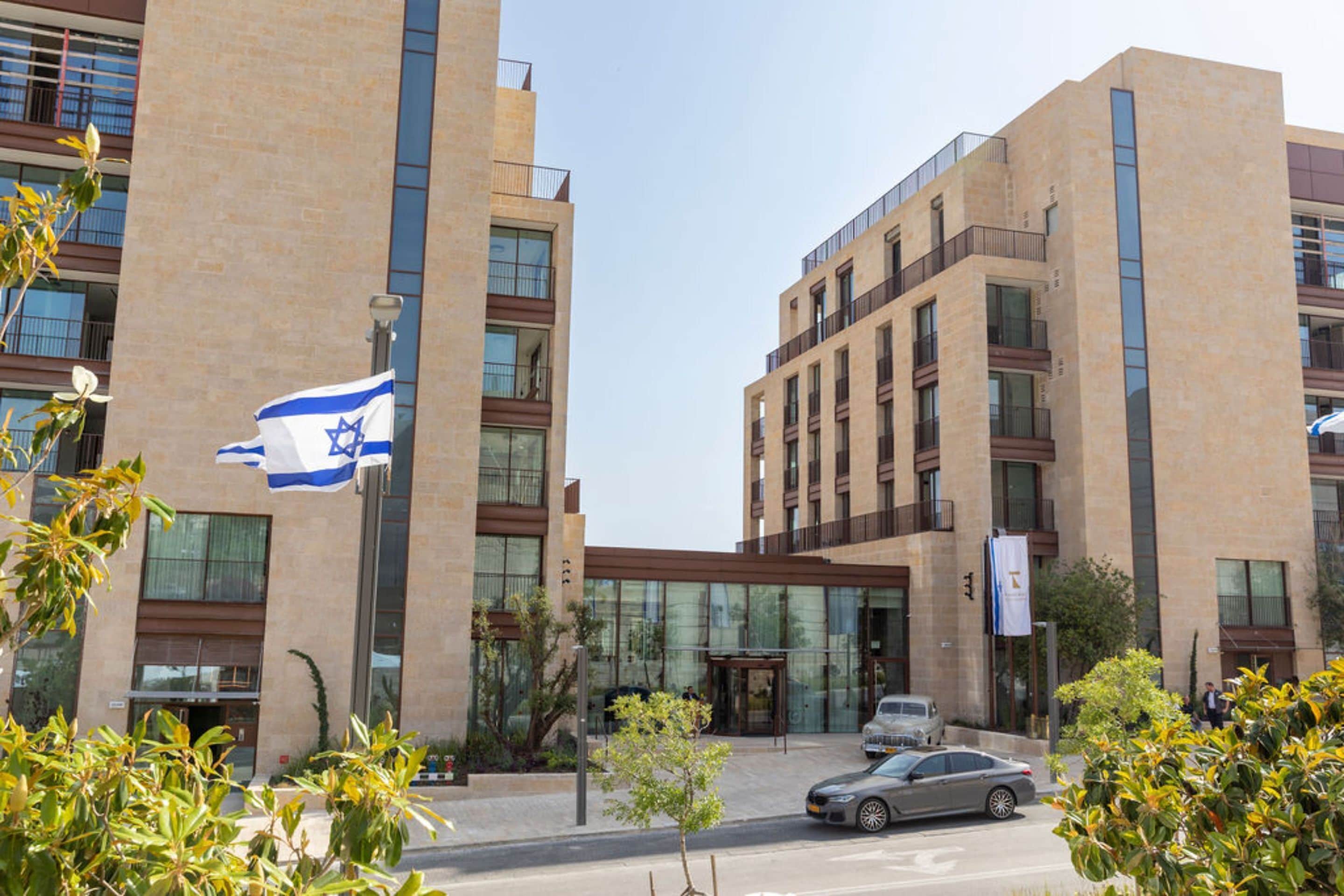 A modern building with a flag, large windows, and a car parked in front.
