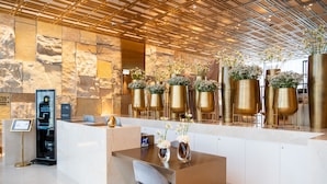A modern reception area with a marble counter, gold vases with flowers, and a digital information kiosk. - Theatron Jerusalem Hotel & Spa - MGallery Collection (Jerusalem)
