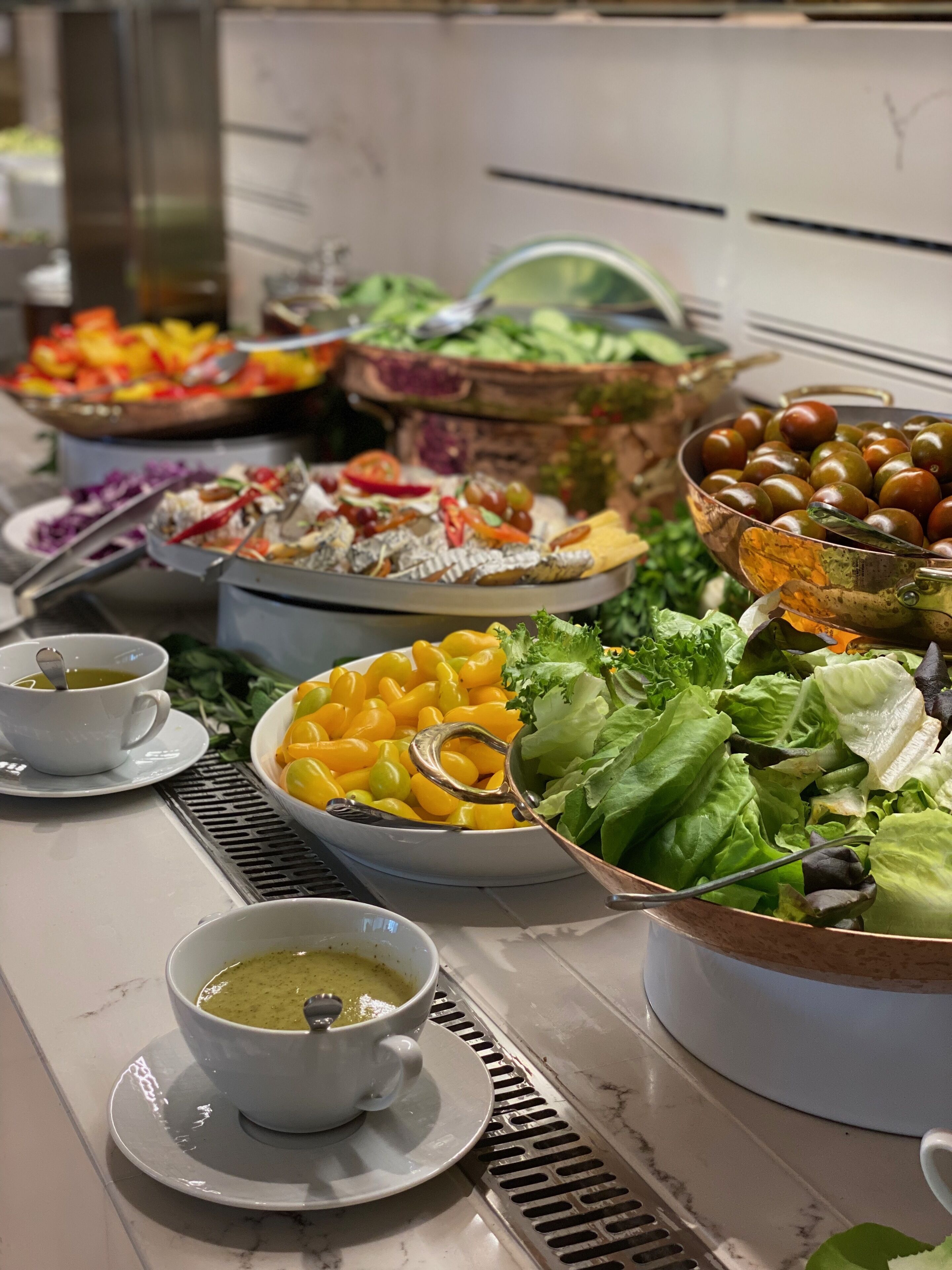 A buffet table with various dishes including salads, fruits, and a bowl of soup.