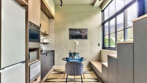 A narrow kitchen with a dining area, featuring a built-in oven, microwave, and a small table with chairs. - The Harri 209 (Cape Town)