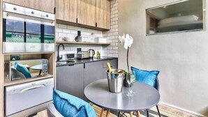 A compact kitchen with modern appliances, a dining area with a round table, and a small window. - The Harri 209 (Cape Town)