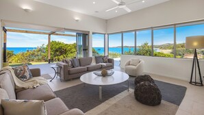 A spacious living room with a large window offering a view of the sea, a ceiling fan, and a modern coffee table.
