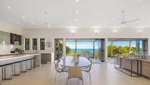 A spacious modern kitchen with a large island, a dining area with a view of the ocean, and a cozy seating area with a view of the greenery.