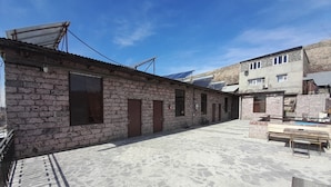 Une cour bordée de bâtiments en pierre, une porte en métal et des panneaux solaires sur le toit.