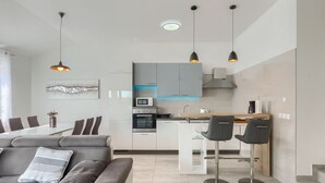 A modern kitchen with white cabinets, a built-in microwave, and a coffee machine. There is a dining area with a gray sofa and a glass table. - Apartment 2217/65764 (Istria - Medulin), 1200m from the beach (Medulin)