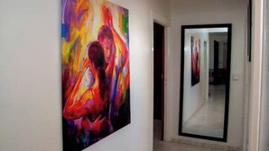 Un couloir avec une grande peinture abstraite sur le mur de gauche et une porte de placard à miroir sur le mur de droite.