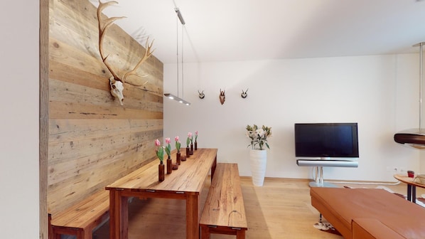 Un salon moderne avec un mur en bois, une longue table en bois ornée de vases de fleurs, un téléviseur à écran plat et un banc.