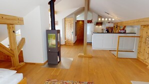 A cozy loft bedroom with a wooden ceiling, a built-in fireplace, and a large window. - Renovated small loft furnished in alpine style perfect for couples or families. (Pontresina)