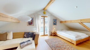 Un dormitorio acogedor en el ático con techo de madera, cama, sofá y ventana con cortinas.