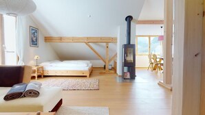 A cozy bedroom with a bed, a wooden ceiling, a large window, and a wood-burning stove. - Renovated small loft furnished in alpine style perfect for couples or families. (Pontresina)