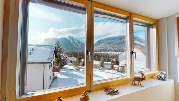 A room with large windows offering a view of snow-covered mountains and a lake. - Renovated small loft furnished in alpine style perfect for couples or families. (Pontresina)