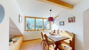 A dining area with a wooden table and chairs, a hanging pendant light, and a window with a view of snow-capped mountains. - Renovated small loft furnished in alpine style perfect for couples or families. (Pontresina)