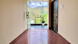 A hallway with a glass door leading to a balcony with a mountain view. - Tapovan New Residency (5 minutes walk to Laxman jhula) (Narendranagar)